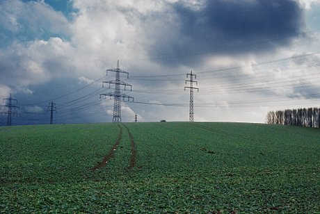 Foto: Feld mit Traktorspuren und Hochspannungsmasten