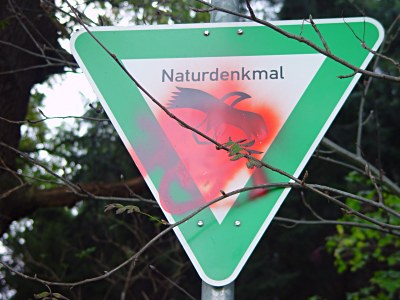 Grünes Hinweisschild mir der Aufschrift Naturdenkmal. Ein Sprayer legte roten Font an. Gesichtet in Birkendahl-Aufderhöhe-Solingen